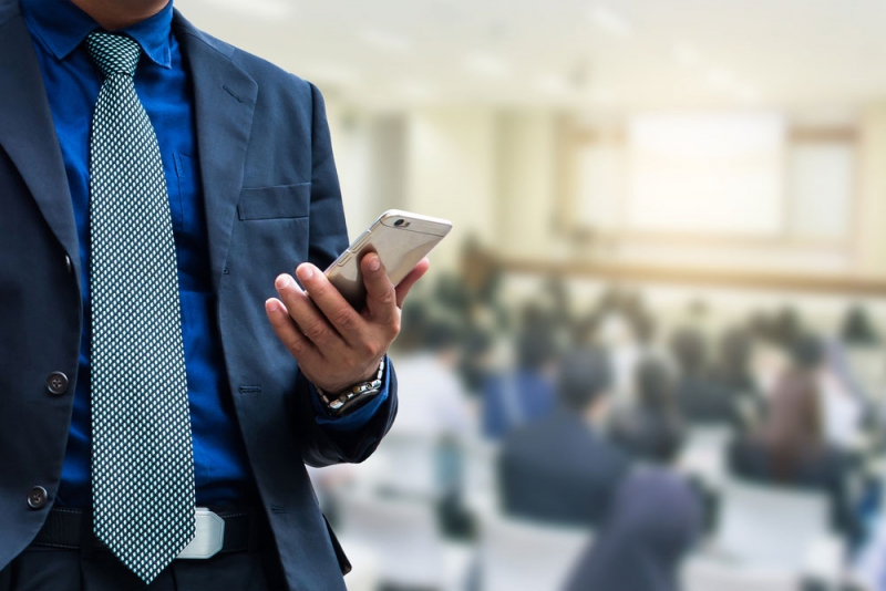 CSG Manager in suit and tie holing smart phone at Continuing Education Class